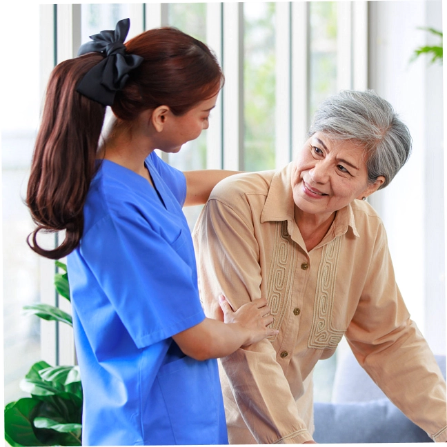 A female caregiver assisting an elderly woman to stand