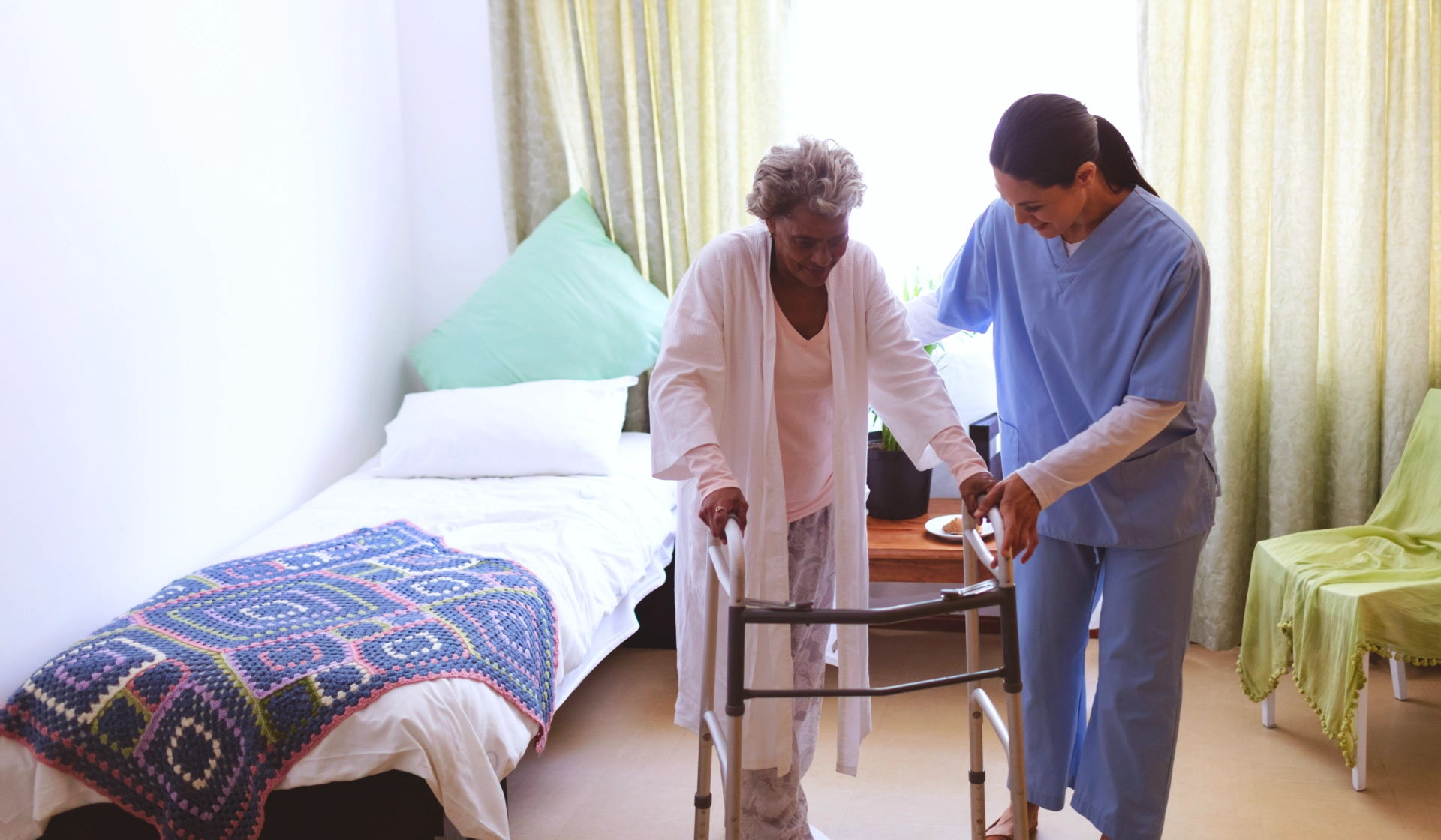 A female caregiver assisting an elderly woman to walk