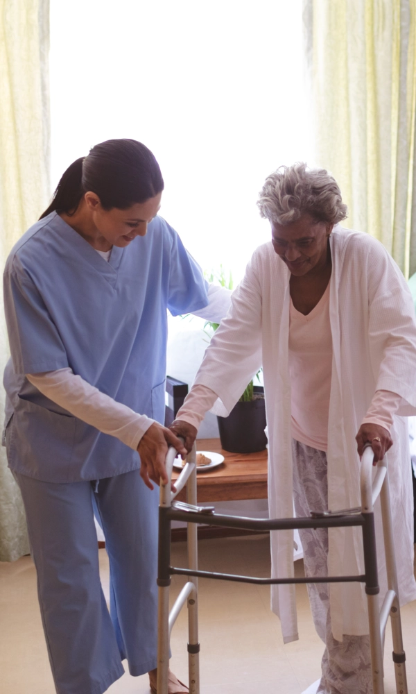 A female caregiver assisting an elderly woman to walk