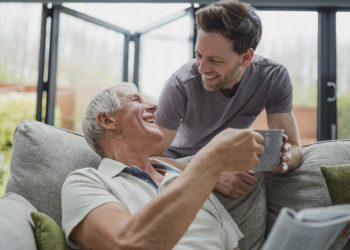 A male giving a cup of coffee to an elderly man