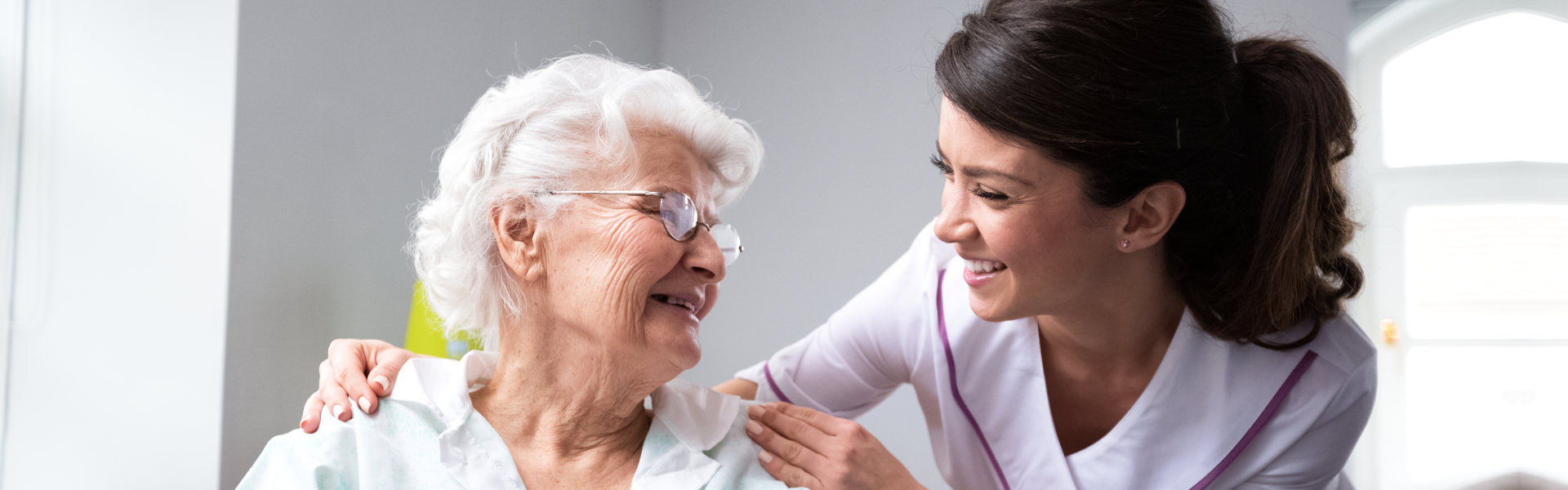 An elderly woman and a female caregiver looking at each other