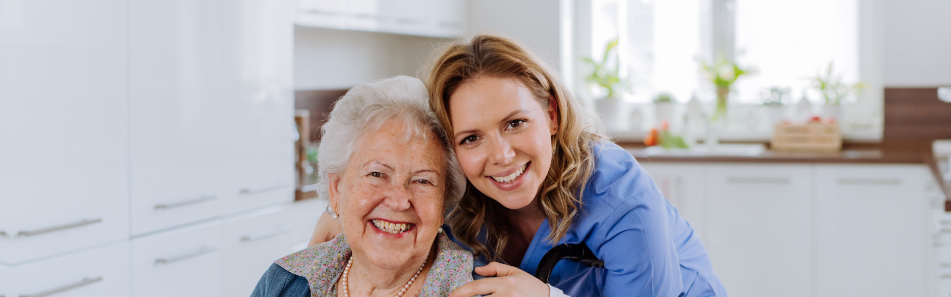 An elderly woman sitting on a wheelchair and a female caregiver hugging her