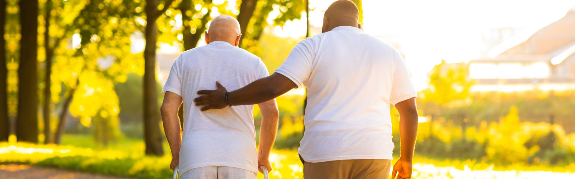 A male assisting an elderly man to walk outside