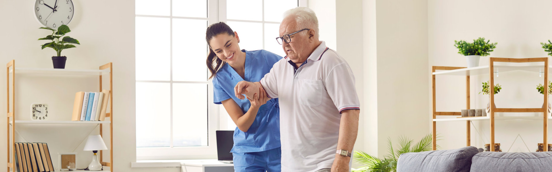 A female caregiver assisting an elderly man to walk