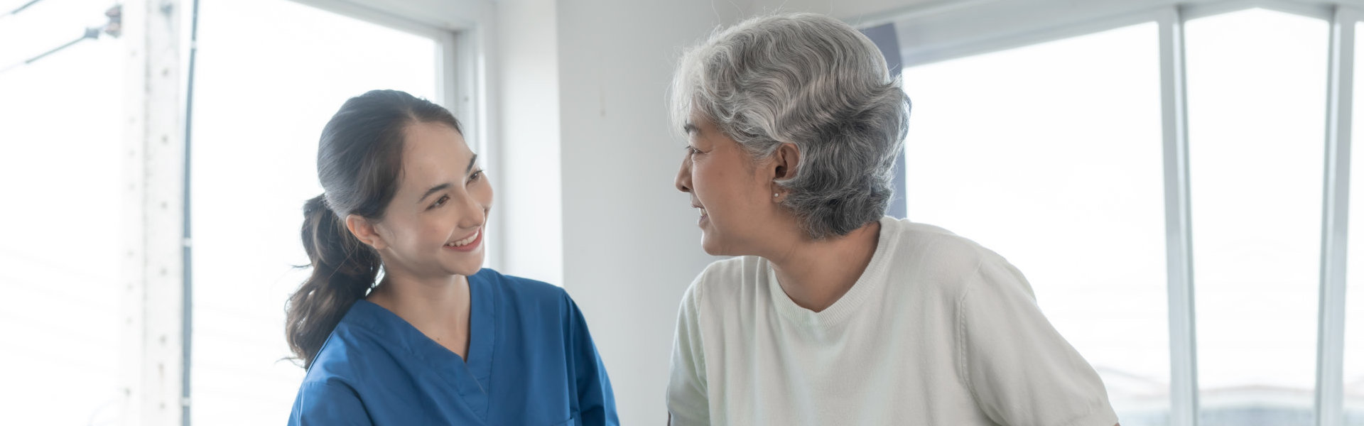 A female caregiver assisting an elderly woman to stand