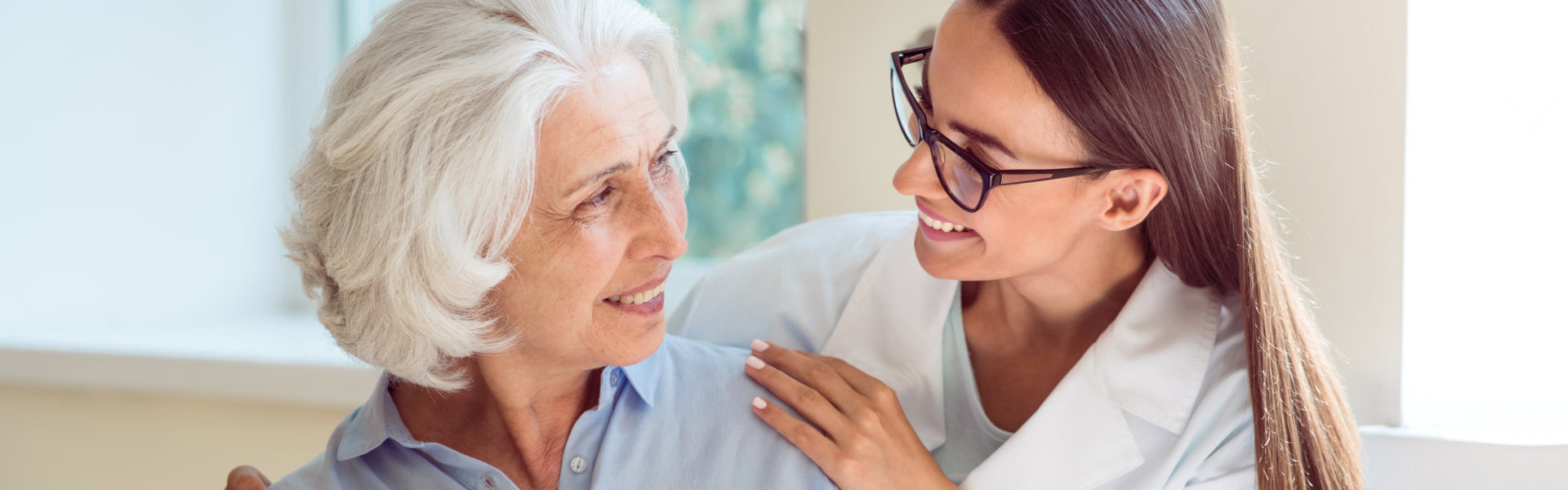 An elderly woman and a female caregiver looking at each other